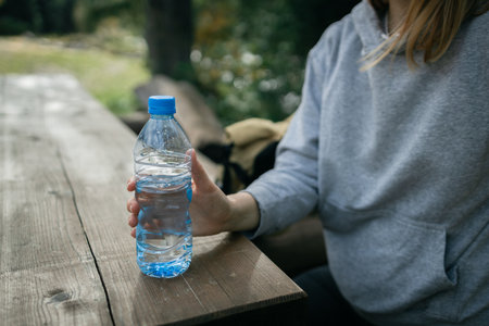 Beautiful woman sitting on a wooden bench at mountain top and contemplating landscape. Woman traveler Female mountaineer looking at beautiful view with a water bottle in hand. Adventure, travel, tourism.の写真素材