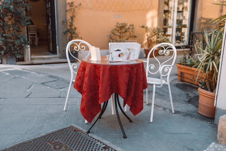 Round wooden table with a red holiday tablecloth and cozy white chair at street cafe. Vacant restaurant furniture on the terrace outdoors.Pisa Italy city. High quality photoの写真素材
