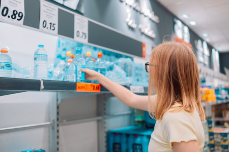 Woman with bottle drinking water in shop. Young blonde cheerful woman picks out a bottle of drinking...