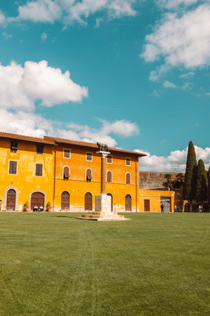 Pisa, Italy - March 18, 2023: Palazzo dellOpera palace, Angelo Caduto statue, Lupa capitolina monument on square with green grass lawn, blue sky white clouds background in sunny day, Tuscany. High quality photoのeditorial素材