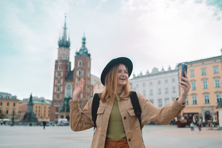 Young stylish woman tourist making selfie photo on Market Square in Krakow, Traveling Europe in spring. St. Marys Basilica. High quality photoの写真素材