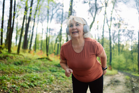 Fitness, health and a running senior woman on a road through a forest or park for cardio and endurance. Exercise, mockup and workout with a mature female runner or athlete training outdoor in nature. High quality photoの写真素材