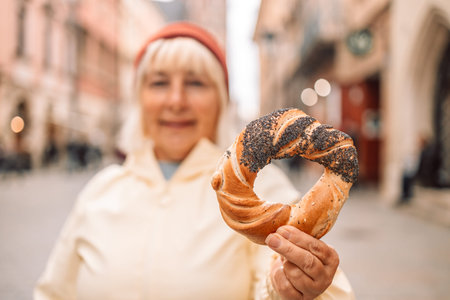 Senior woman holding prezel, traditional polish snack against old city center view in Krakow.
