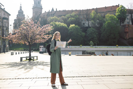 Traveller woman walking near famous old Wawel Royal Castle in Krakow holding tourist map shows the direction of the path. Travel and active lifestyle concept. Spring Cherry blossoms, pink flowersの写真素材