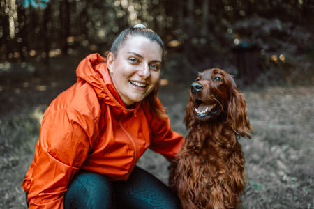 Happy caucasian woman hiker hiker walks with her cute Irish Setter dog on a walk in a summer forest. High quality photoの写真素材