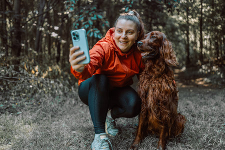 Happy caucasian girl hiker hiker takes a selfie with her cute Irish Setter dog on a walk in a summer forest, adventure travel and discoveryの写真素材