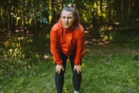 Tired caucasian woman is holding her knee joint in excruciating pain at uphill road. Adventure travel and discoveryの写真素材