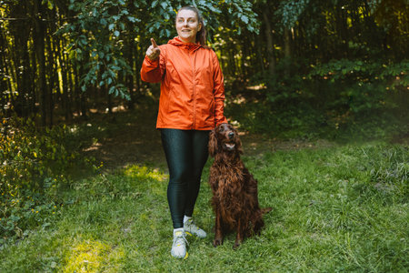 Happy caucasian woman hiker hiker walks with her cute Irish Setter dog on a walk in a summer forest. High quality photoの写真素材