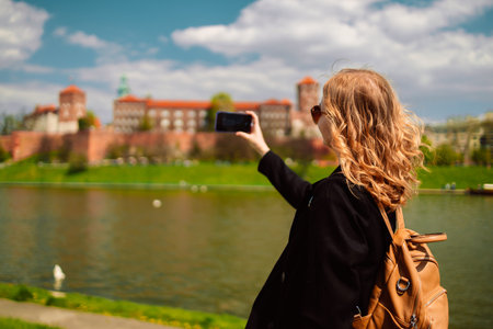 Young blonde woman tourist with stylish clothes and sunglasses making photo the famous Wawel Castle and Wawel cathedral in Krakow city. Happy vacations in Poland. High quality photoの写真素材