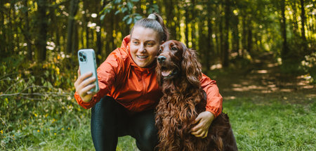 Happy caucasian girl hiker hiker takes a selfie with her cute Irish Setter dog on a walk in a summer...