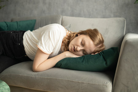 Peaceful young 30s woman lying barefooted on the sofa and closing her eyes while falling asleep with one hand touching the floor. High quality photoの写真素材