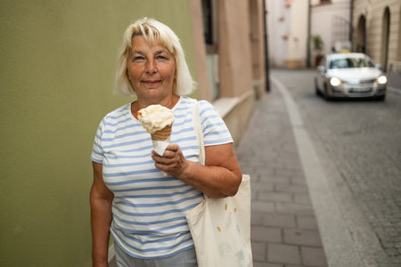 Happy senior 50s woman with delicious ice cream in waffle cone outdoors. Space for text. High...