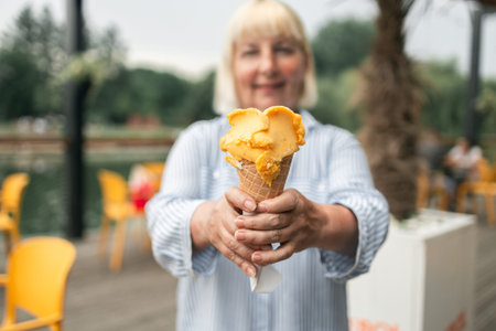Happy smiling senior woman dressed in stylish clothes eating ice cream in the city summer outdoors...