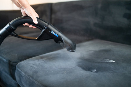 Cleaning service company employee removing dirt from furniture in flat with professional equipment. Female housekeeper arm cleaning sofa with washing vacuum cleaner close up. High quality photoの写真素材