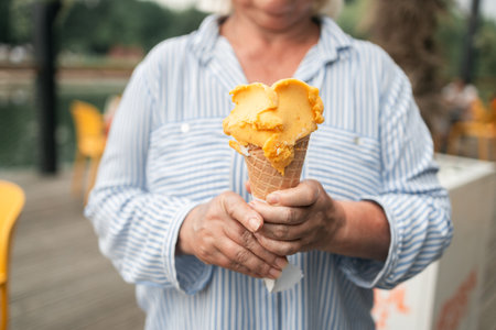 Happy smiling senior woman dressed in stylish clothes eating ice cream in the city summer outdoors cafe interior. High quality photoの写真素材