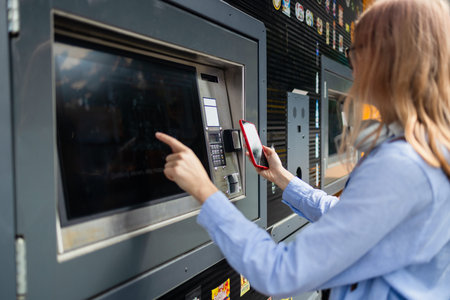 Beautiful woman picking up a package from a smart electronic steel parcel locker box, automatic...