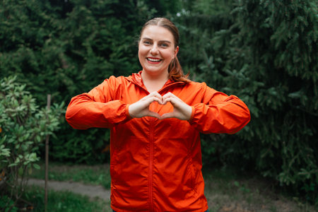 Photo of fitness cheerful charming young sportive woman show fingers heart symbol love isolated over park background. High quality photoの写真素材