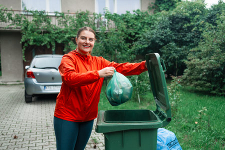 Caucasian woman sorting garbage, throwing a used paper bag in a small recycle bin at outdoor near a home . High quality photoの写真素材