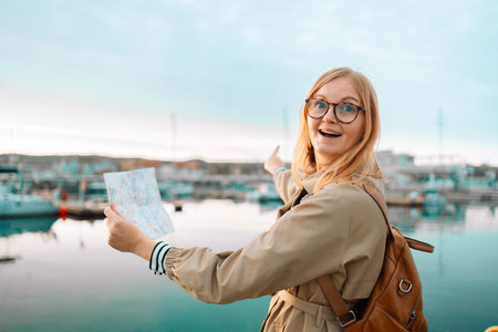 Young adult tourist woman reading map hiking trip looking to find place to go on the pier near the expensive yachtsの写真素材