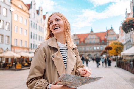 Attractive young female tourist holding a paper map on central square in Gdansk old town. Traveling...