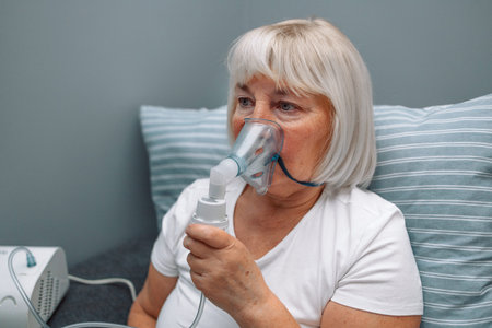 Sick upset caucasian senior woman with an inhaler. Unhealthy female doing inhalation at home, she...