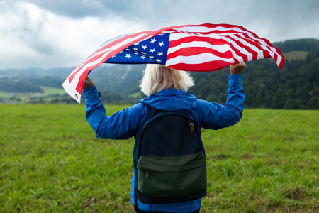 Happy senior 50s woman walking and waving American flag. Patriotic holiday. Female with American flag. USA celebrate 4th of July. Independence Day concept. High quality photoの写真素材