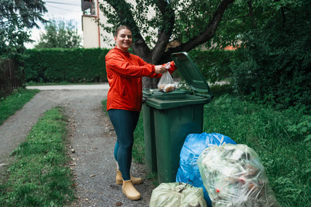 Caucasian woman sorting garbage, throwing a used paper bag in a small recycle bin at outdoor near a home . High quality photoの写真素材