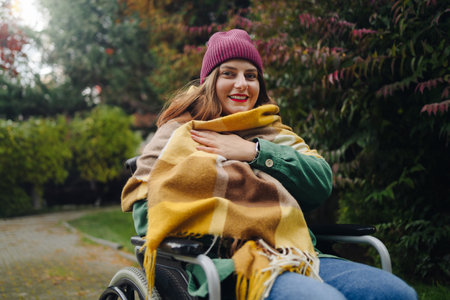 Happy smiling cheerful Caucasian woman in stylish clothes on a wheelchair relaxing alone in autumn park. Female looking at cameraの写真素材