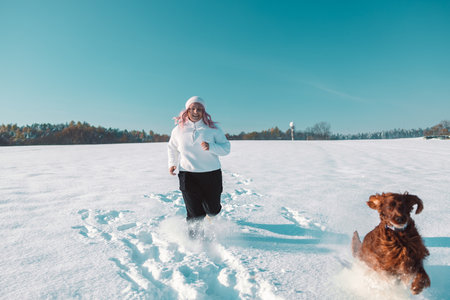 Active Irish Setter dog with woman running slow motion footage during the snowy walking, having fun in winter park during beautiful sunny winter day. High quality FullHD footageの写真素材