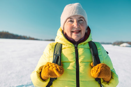 North 60s senior woman relaxing on the hill. Woman drinking hot tea from thermo cup and enjoying panorama city park view. Happiness, winter holidays, tourism, travel and people concept.の写真素材