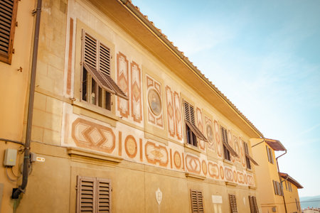 The facade of a building in sunlight in Florence. Open wooden shutters on the windows. tarin patterns ornaments on the pastel wall of the building, Italy. High quality photoの写真素材