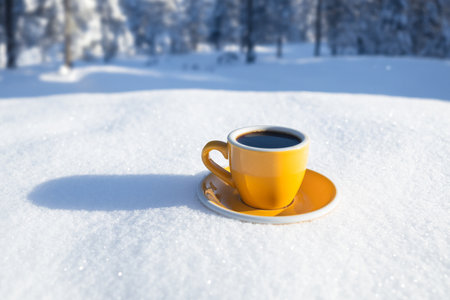 Winter background. Yellow cup with hot coffee or tea stand on the snow outdoor at sunny day with cold weather outdoors.の写真素材