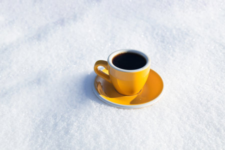 Winter background. Yellow cup with hot coffee or tea stand on the snow outdoor at sunny day with cold weather outdoors.の写真素材
