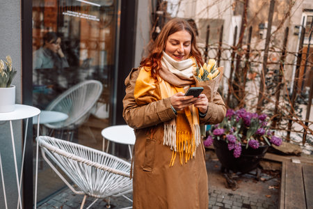 Sensual brunette in fashionable clothes sits with a bouquet of flowers at a table in a cafe and waits for her man. High quality photoの写真素材