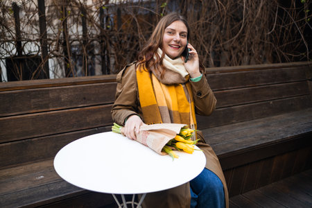 Sensual brunette in fashionable clothes sits with a bouquet of flowers at a table in a cafe and waits for her man. High quality photoの写真素材