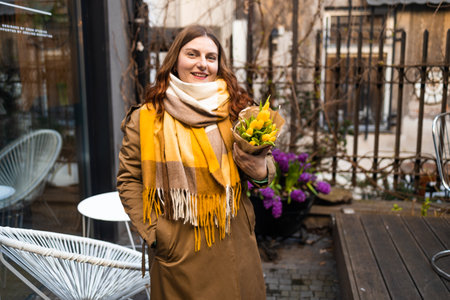 beautiful young woman in spring style outfit smiling happy walking with flowers in city street . High quality photoの写真素材