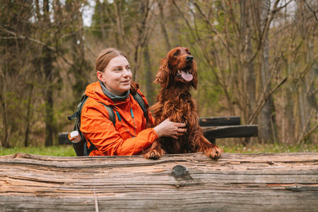 Young happy woman with sport backpack resting traveling with dog. A young female hugs her beloved dog. Girl and irish setter in the spring forest at sunset. High quality photoの写真素材