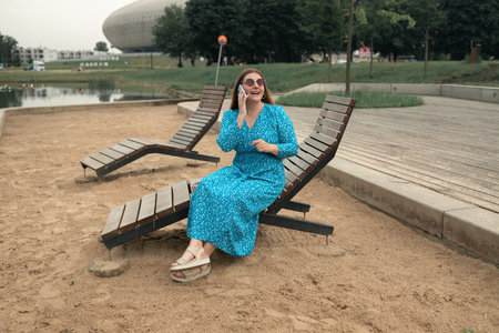 Young pretty woman model in stylish dresses talk by mobile cell phone look aside standing on summer in spring park outdoors. Urban lifestyle concept. High quality photoの写真素材