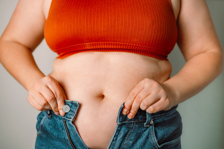 Fat woman trying to zip up her jeans pants. Womens health. Women body fat belly. Obese woman hand holding excessive belly fat. Diet lifestyle concept, healthy stomach muscle.の写真素材