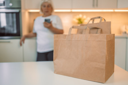 Online home food delivery. Woman checking her online order list on her phone. Young woman unpacking boxes of food at home. Start of a healthy life.の写真素材