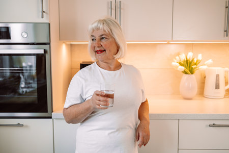 Smiling pretty woman holds a glass of water leaning on kitchen desk. High quality photoの写真素材