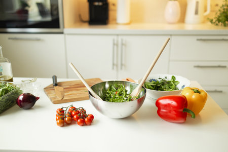 A bowl with a salad of fresh vegetables, tomatoes, arugula and spinach on the kitchen table. Healthy vegetarian salad on the white table in the kitchenの写真素材
