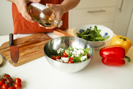 Woman seasons a vegetable salad while preparing food in the kitchen. Unrecognizable chef adds olive oil while preparing a vegetarian meal at home. Healthy eating concept.の写真素材