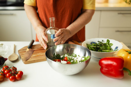 Close up of senior woman is preparing vegetable salad in the kitchen.Female adding arugula to salad. Healthy Food. Vegan Salad. Diet. Dieting Concept. Healthy Lifestyle. Cooking At Home. Prepare Food. Cutting ingredients on tableの写真素材