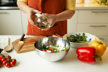 Woman seasons a vegetable salad while preparing food in the kitchen. Unrecognizable chef adds olive oil while preparing a vegetarian meal at home. Healthy eating concept.の写真素材