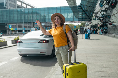 Happy traveling Caucasian woman tourist passenger is using mobile application to call pick up taxi at airport terminal for transportation during her vacation travel and long weekend holiday. High quality photoの写真素材