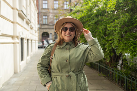 Portrait of a beautiful Caucasian female in a green coat, carrying a walking bag, smiling in a good mood in the city outdoors. High quality photoの写真素材