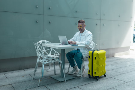 Happy traveling Caucasian man in stylish clothes uses mobile smartphone and laptop, checking trip destination on Internet. Male waiting at flight gates for plane boarding, smiling have a vacation trip. High qualityの写真素材