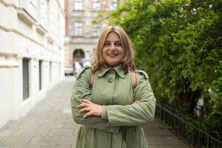 Portrait of a beautiful Caucasian female in a green coat, carrying a walking bag, smiling in a good mood in the city outdoors. High quality photoの写真素材