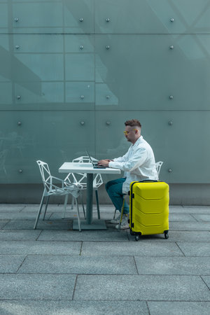 Happy traveling Caucasian man in stylish clothes uses mobile smartphone and laptop, checking trip destination on Internet. Male waiting at flight gates for plane boarding, smiling have a vacation trip. High qualityの写真素材